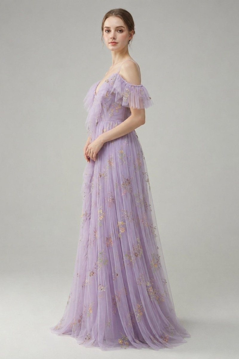 A woman models a lavender off-the-shoulder tulle gown with gold floral embroidery against a neutral gray studio background.