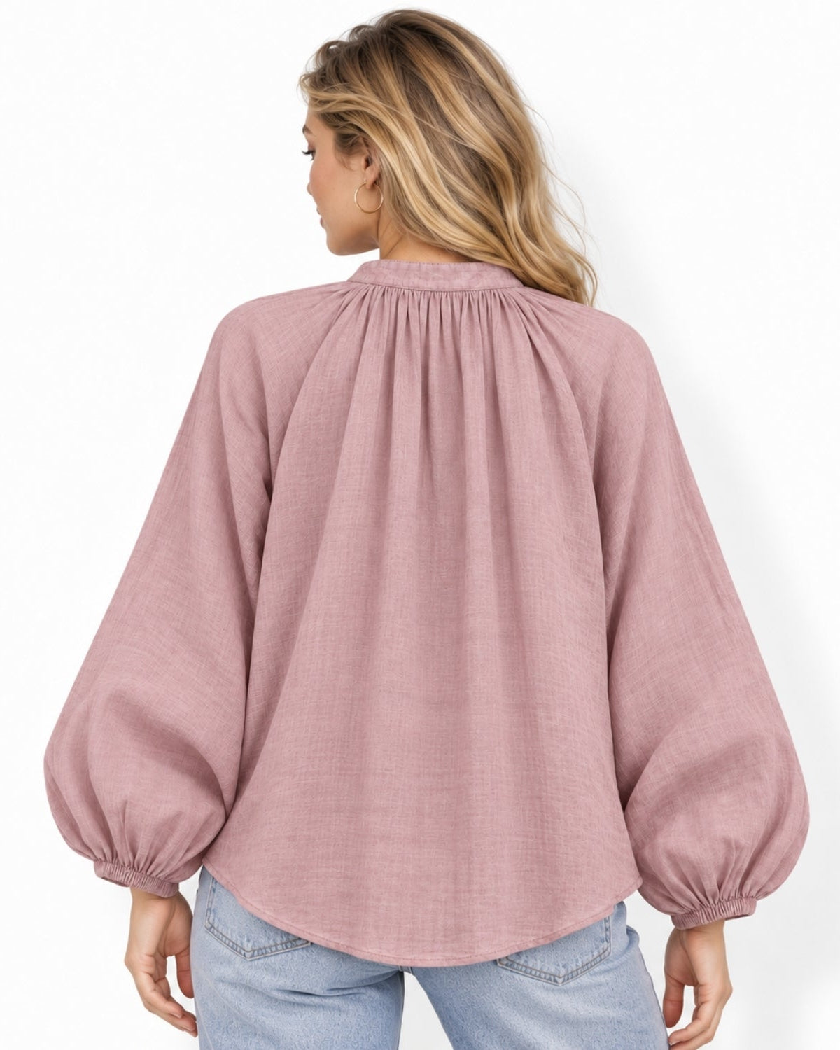 A woman viewed from the back wearing a lavender long-sleeve blouse with a gathered, pleated high neckline and elasticized cuffs, paired with light blue jeans against a plain white background.
