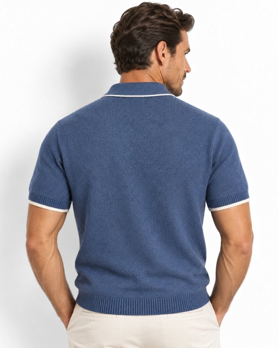 A man viewed from the back wearing a blue short-sleeve knit polo shirt with white trim on the collar and sleeve cuffs, paired with light beige pants, against a plain white studio background.