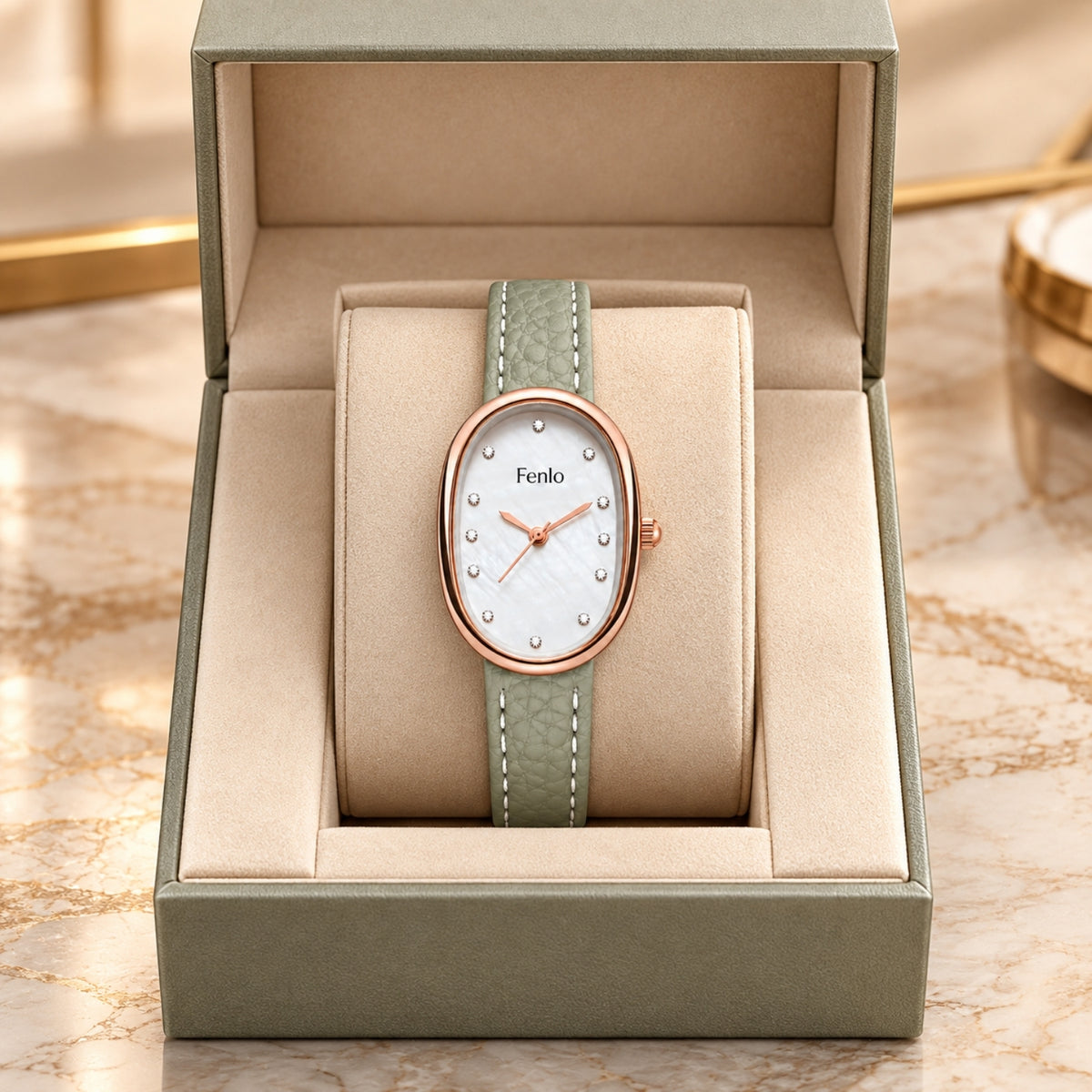 A Fenko oval watch with a light green textured strap and rose gold case, presented inside an open beige watch box on a marble surface.