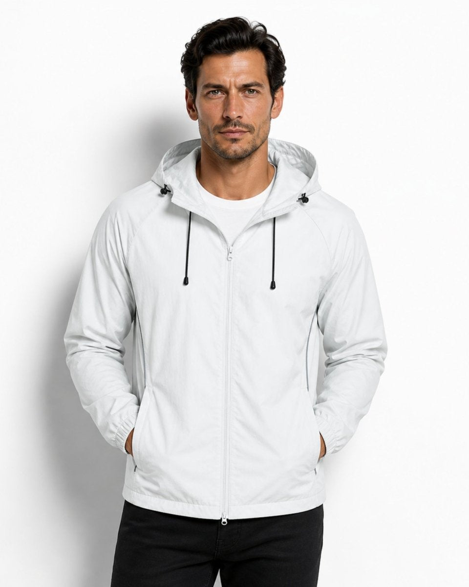 Male model wearing a premium lightweight light grey hooded windbreaker jacket with black drawstrings, hands in pockets, modern athleisure style.