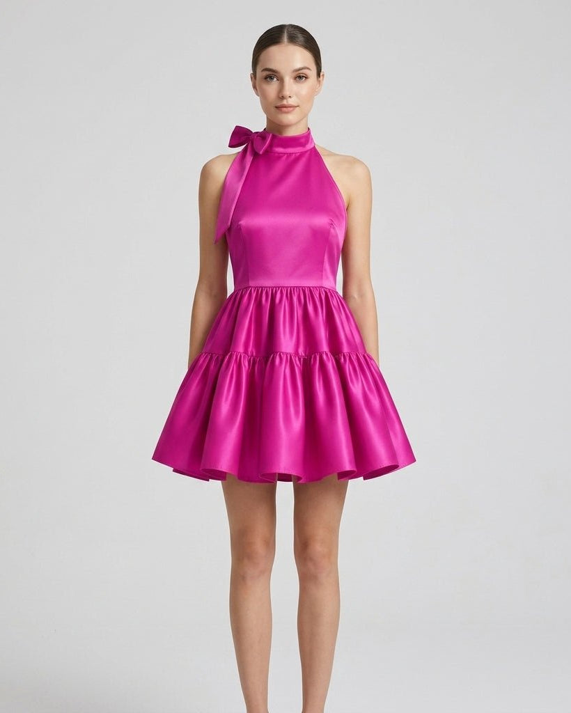 Front view of the magenta fuchsia satin halter neck tiered mini dress with front tie detail worn by a brunette model.