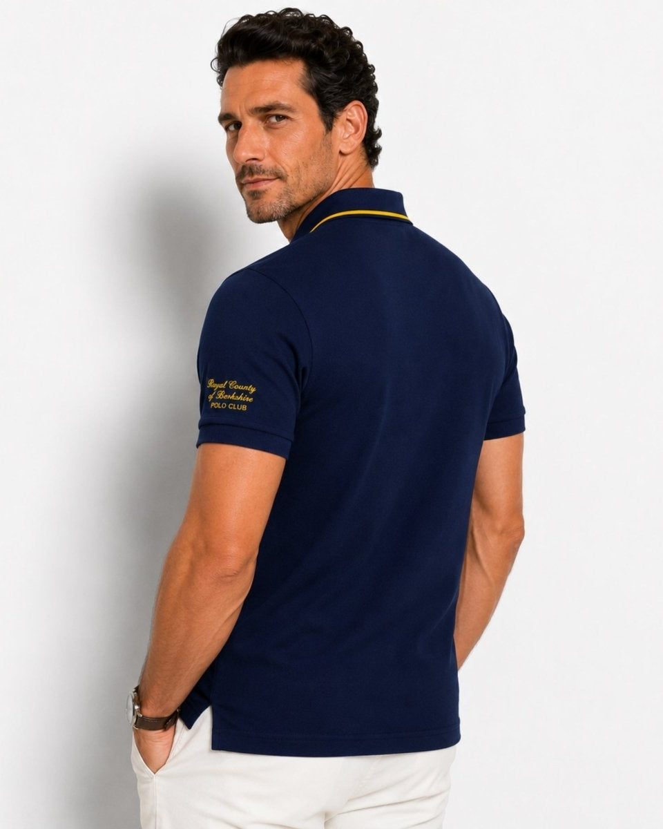 Man wearing a navy blue polo shirt with a brand logo on the back, standing against a light gray background.