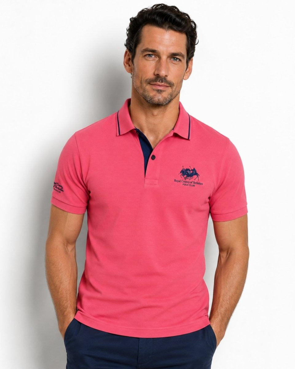 Man wearing a pink polo shirt with a logo on a white background