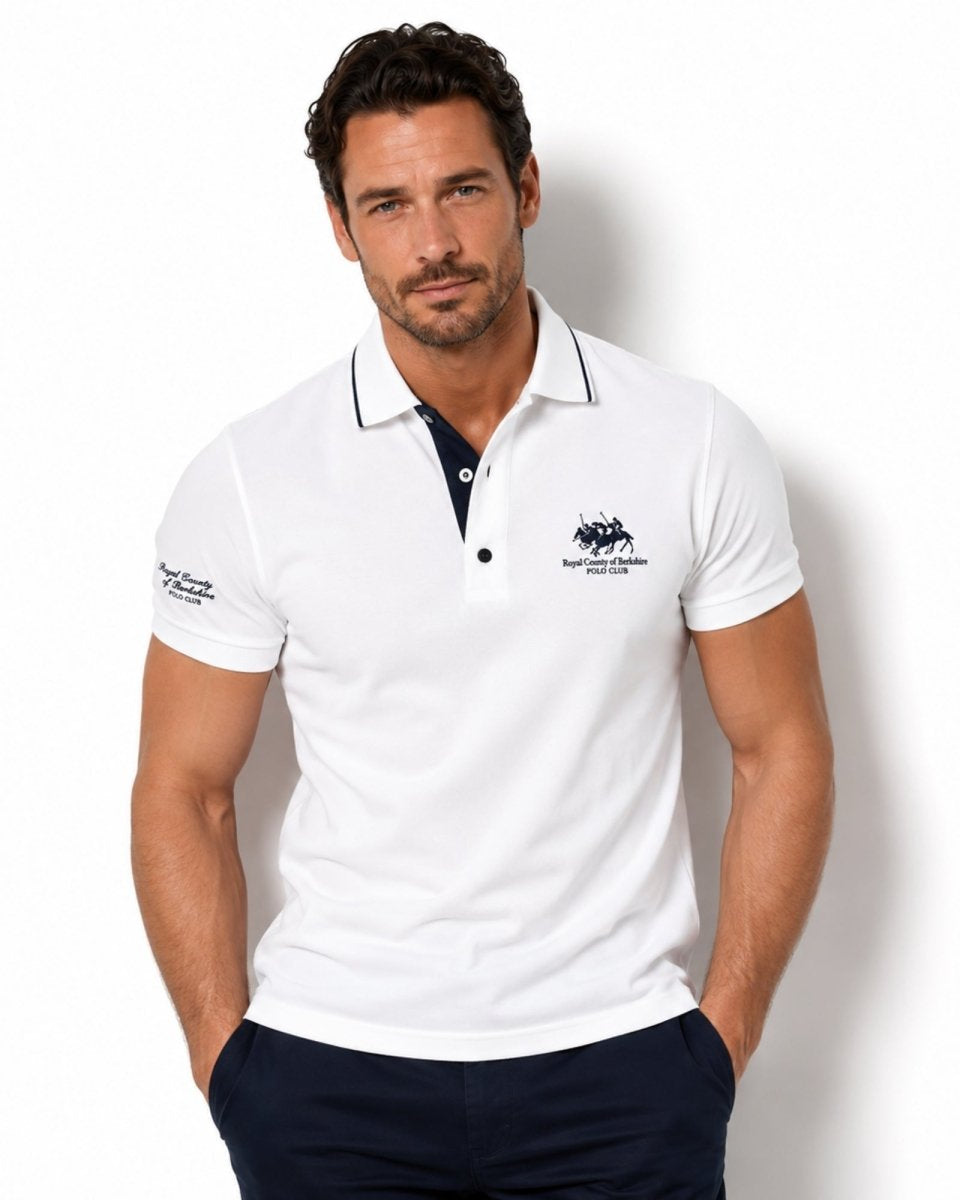 Man wearing a white polo shirt with a logo on a light background