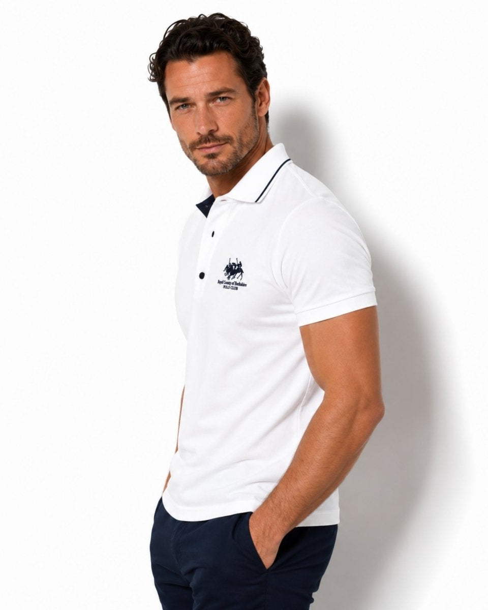 Man wearing a white polo shirt with a logo on a plain background