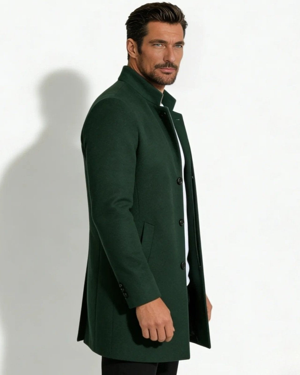 Side profile of a man in a slim fit dark green wool topcoat with a stand collar, showing the coat's silhouette and length.
 