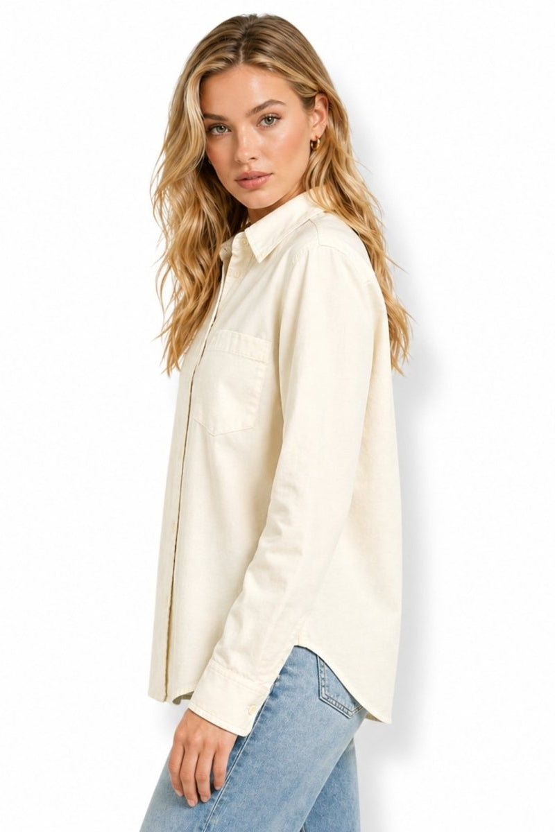 Side profile of a minimalist beige long sleeve button down blouse showing the tailored sleeve drape and relaxed fit over casual denim.