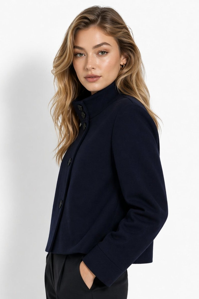 Side profile of blonde woman wearing elegant minimalist navy funnel neck short coat outerwear.