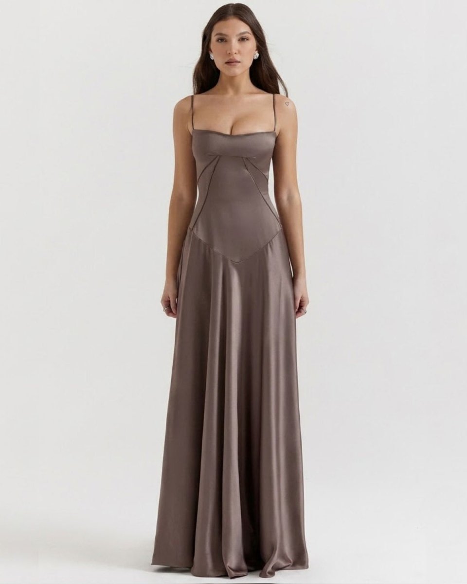 A woman modeling a floor-length satin gown in a muted taupe-brown color against a plain light gray studio background.