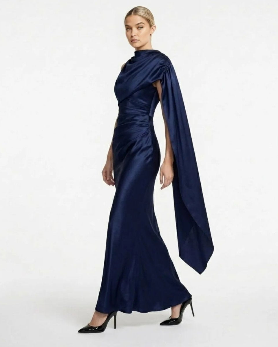 Side profile of a female model wearing the navy blue ruched satin formal dress by showcasing the cape detail.