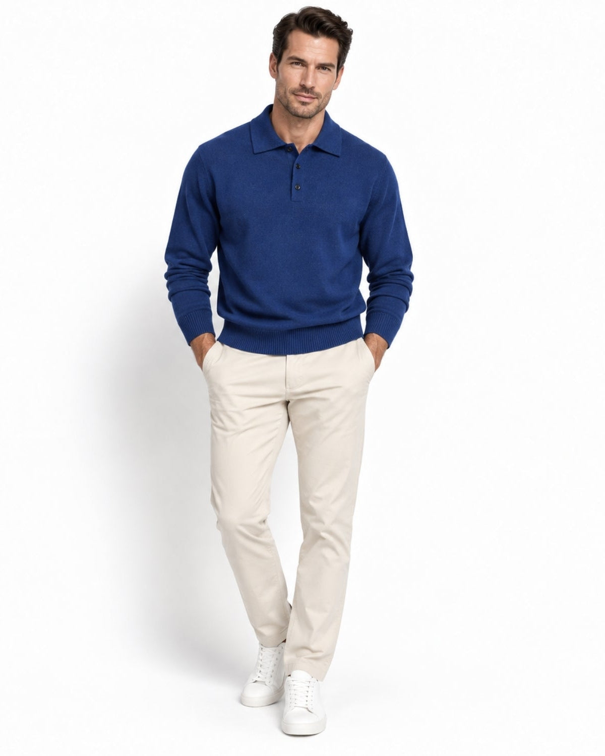 A man modeling a blue long-sleeve polo sweater, paired with beige trousers and white sneakers, standing against a plain white studio background.