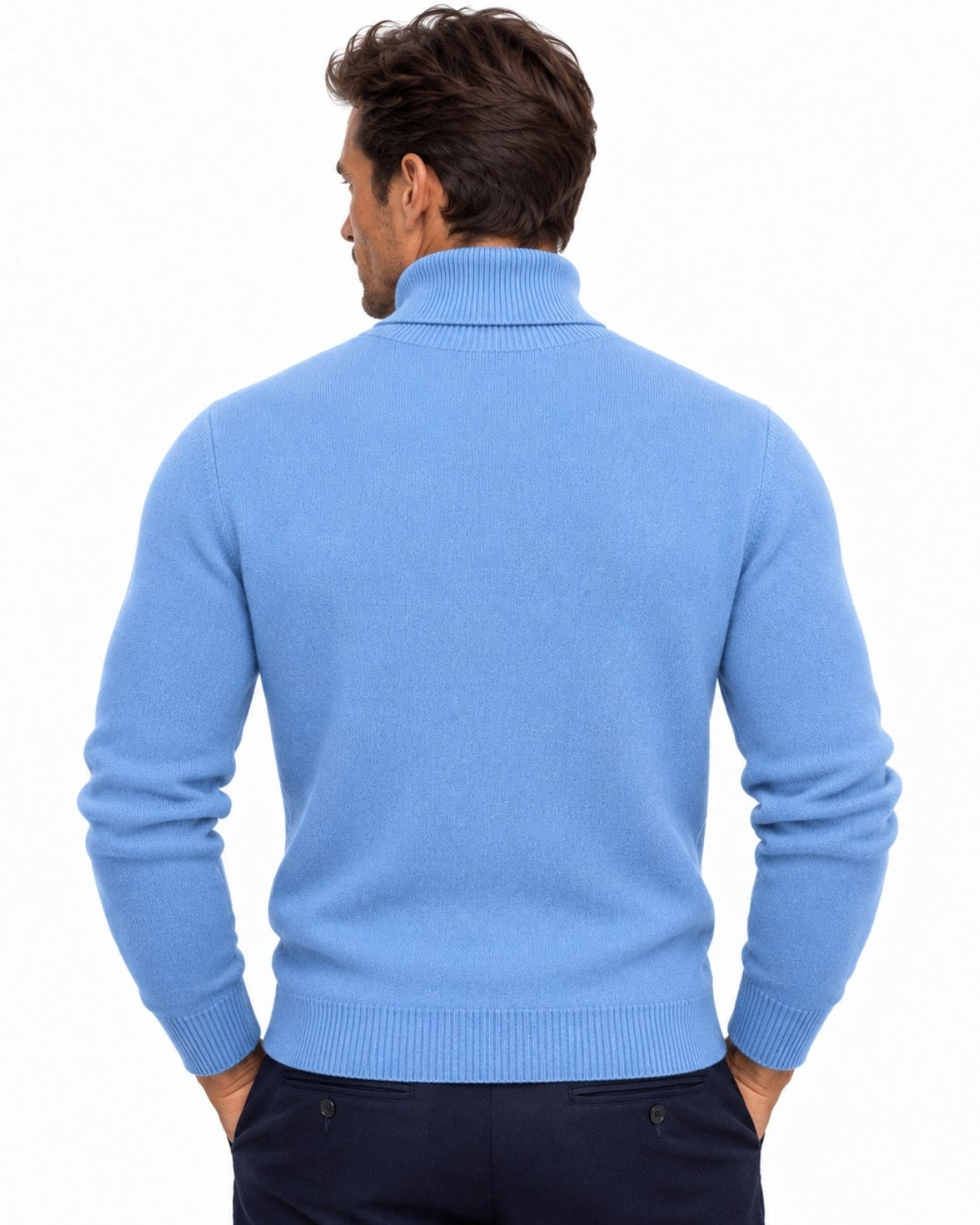 A man viewed from the back wearing a light navy ribbed mock-neck sweater and dark navy trousers, set against a plain white studio background.