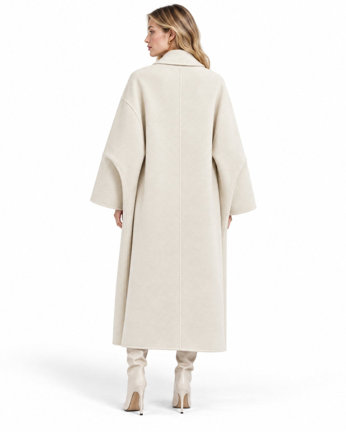 A woman shown from the back wearing a long, oversized cream-colored coat with wide draped sleeves, paired with light beige high-heeled boots, against a solid white background.