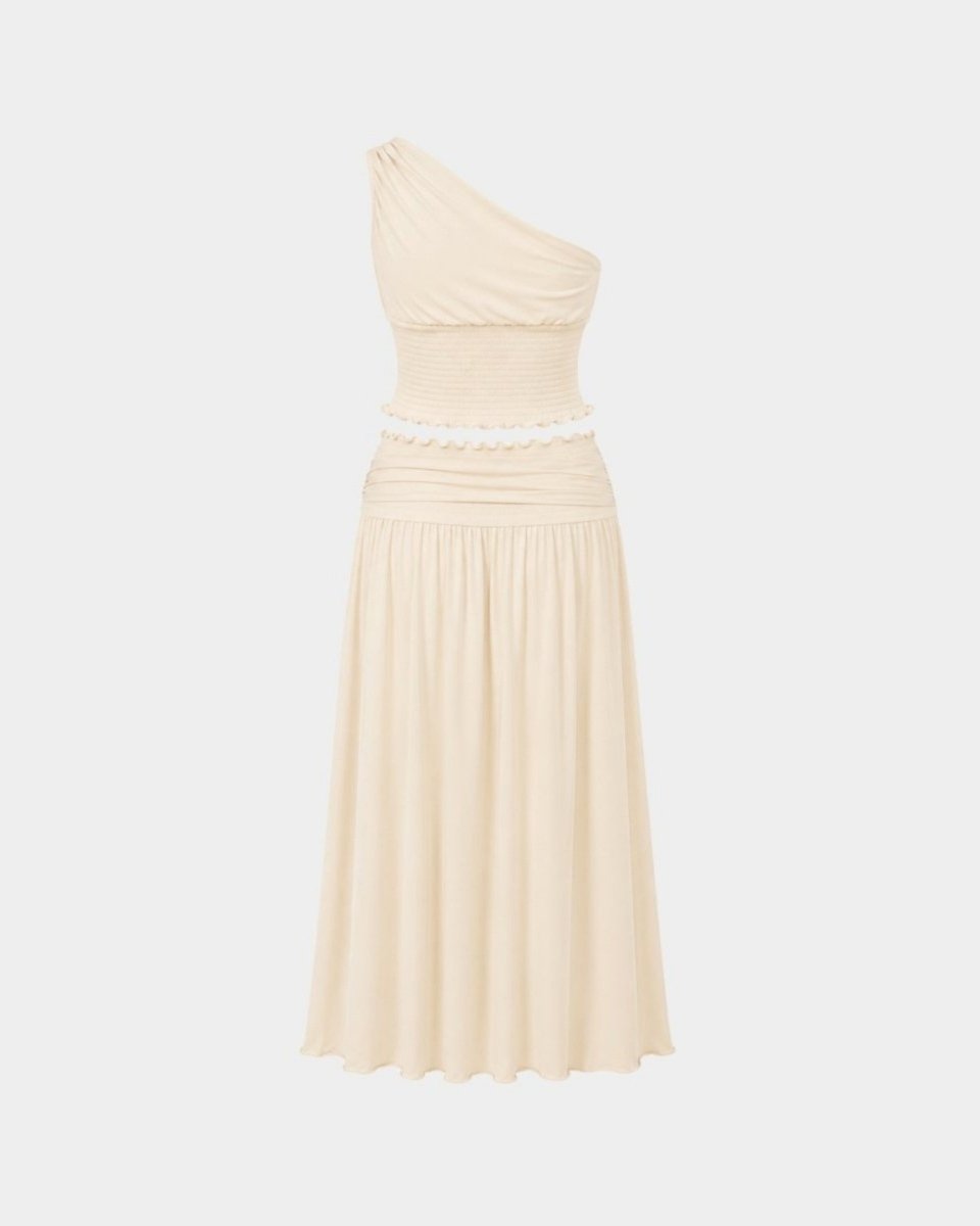 A light beige one-shoulder midi dress with a ruched bodice, a textured waistband with a scalloped edge, and a flowing pleated skirt, shown against a light gray background.