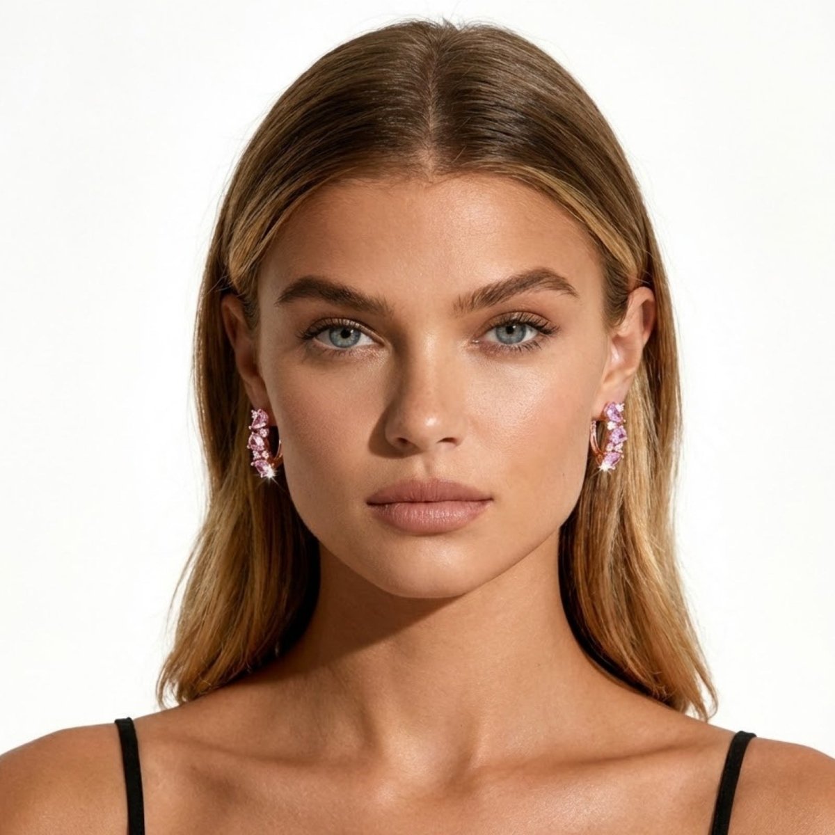 A model with blonde hair and blue eyes looking directly at the camera, wearing Kouvr's Laliana pink sapphire cluster huggie earrings in rose gold.

