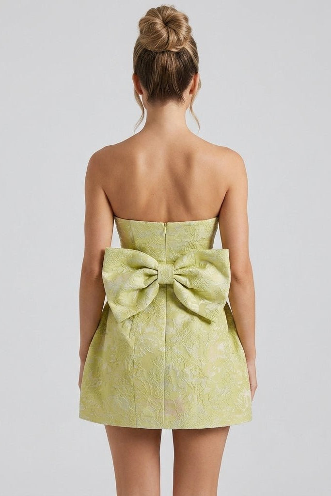 Back view showcasing the oversized statement bow on the yellow textured mini dress