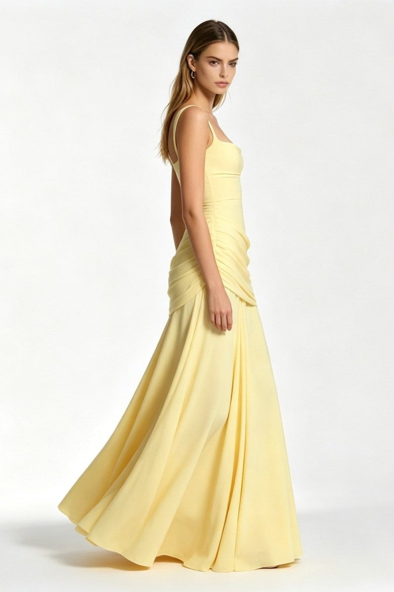 Side profile of a woman twirling in a pale yellow floor-length flowy formal maxi dress featuring asymmetrical draped hip details.