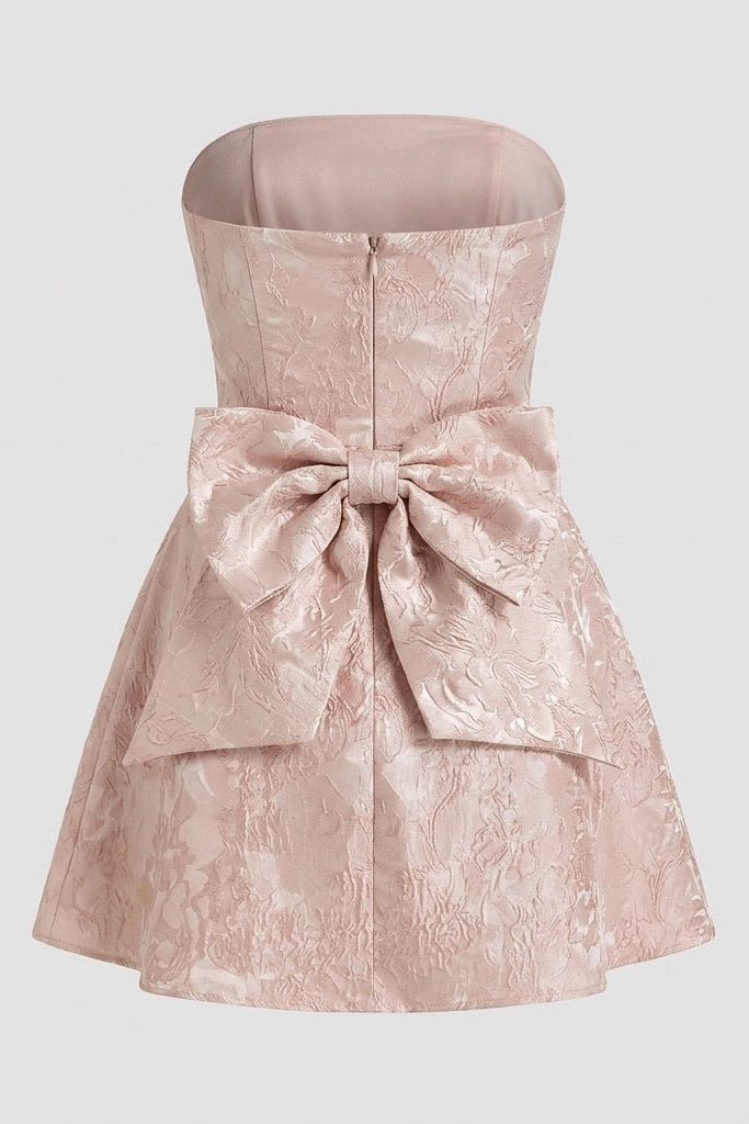 Studio flat lay product back view of a pink formal mini dress showcasing the large structural bow detail.