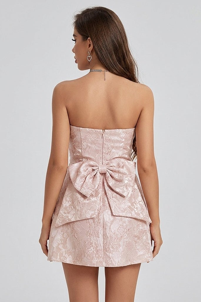 Back view of a pink fit and flare mini dress featuring an oversized architectural statement bow and invisible zipper.