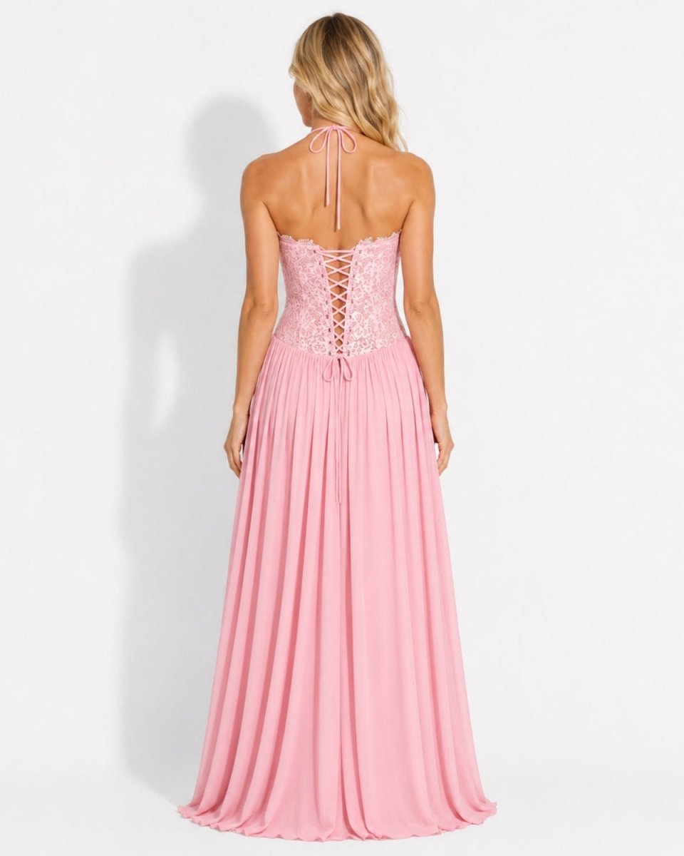 A woman shown from the back wearing a pink strapless maxi dress with lace-up back detailing and a flowing skirt, photographed against a plain light gray studio background.