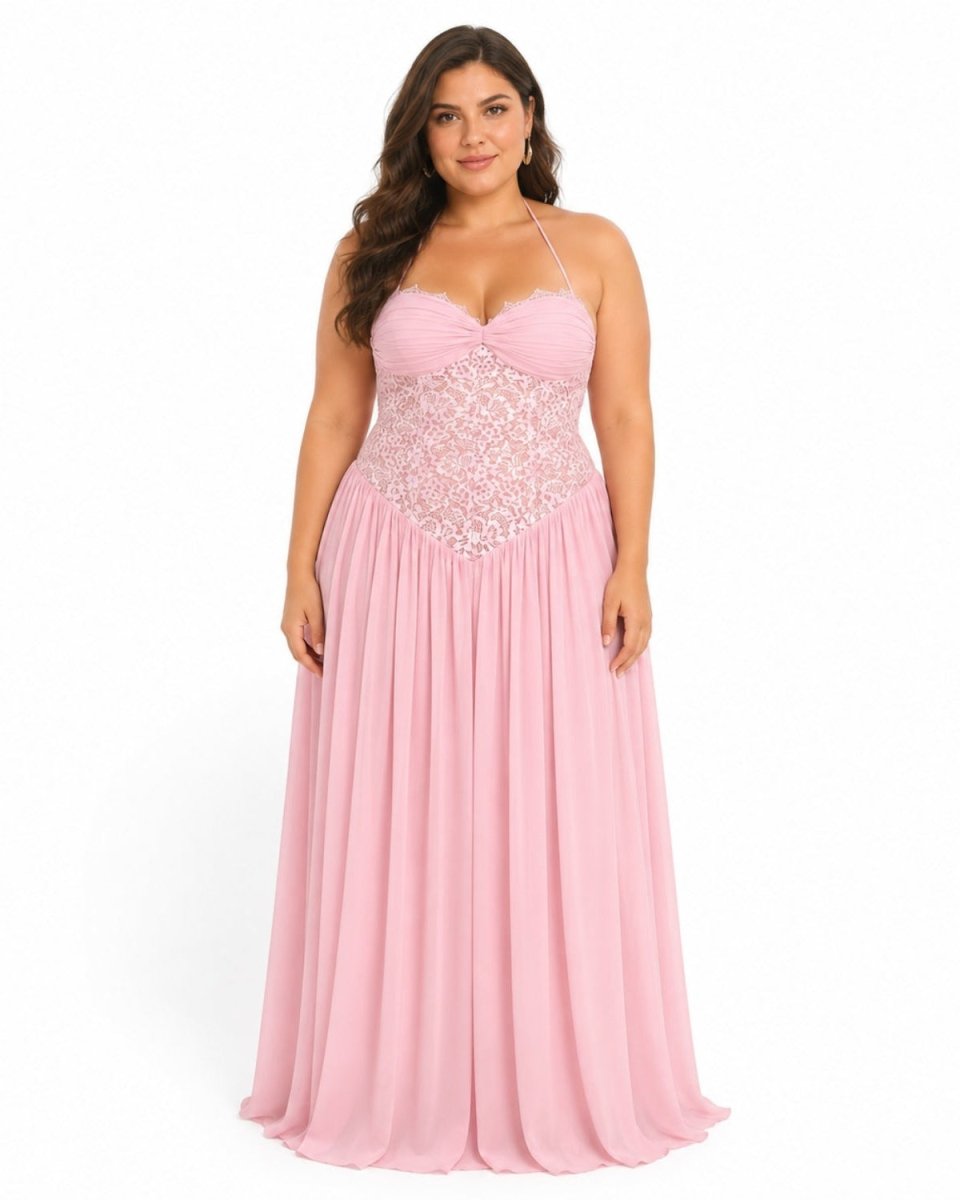 A woman modeling a floor-length pink gown with thin straps, a sweetheart neckline, and a lace-embroidered bodice against a plain white studio background.