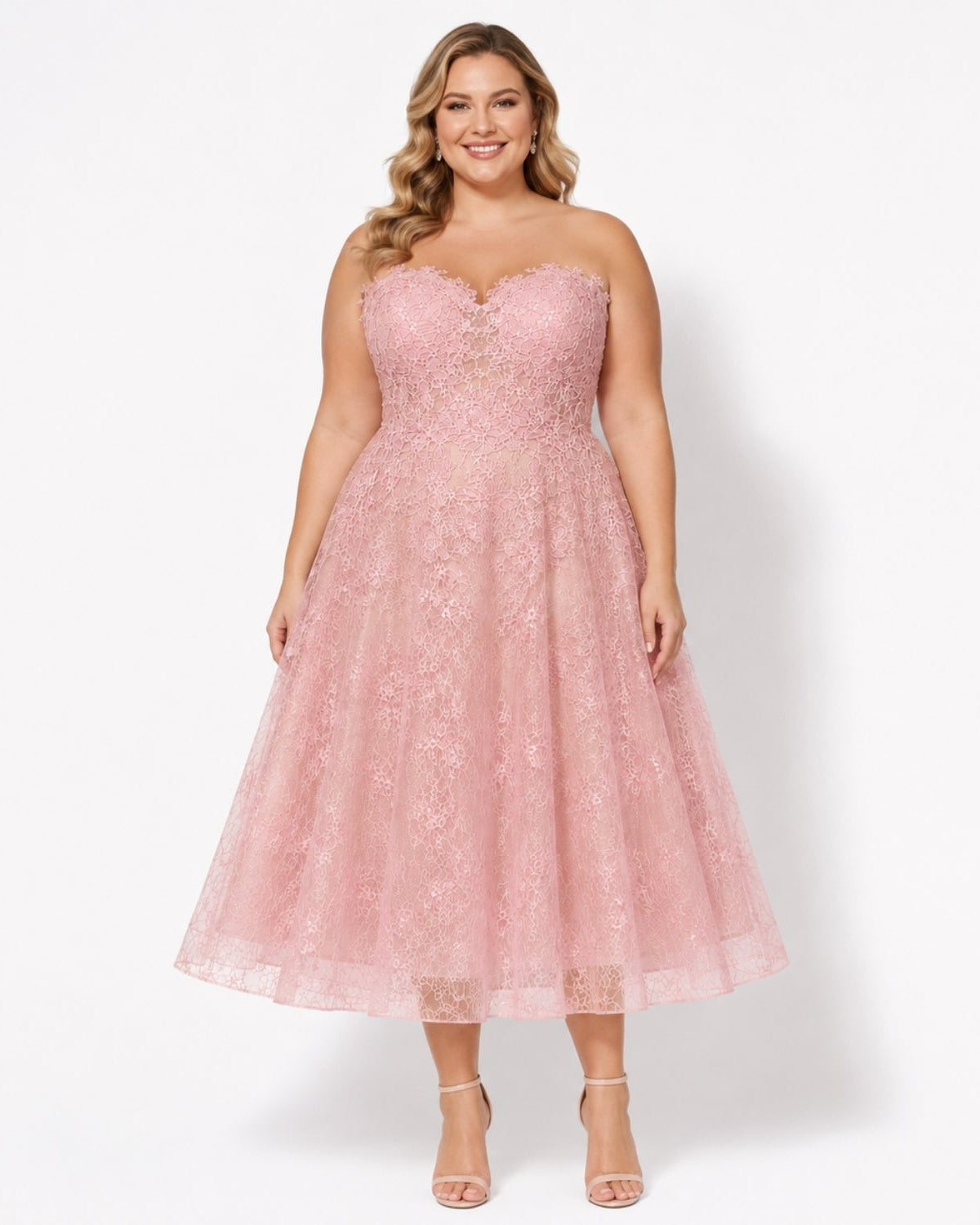 A woman modeling a strapless pink lace and tulle midi dress with a sweetheart neckline, fitted bodice, and flared skirt, photographed against a clean white studio background.
