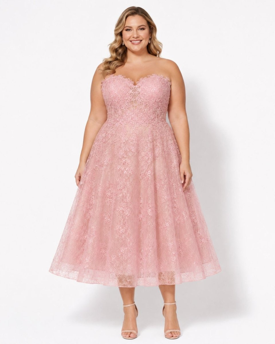 A woman modeling a strapless pink lace and tulle midi dress with a sweetheart neckline, fitted bodice, and flared skirt, photographed against a clean white studio background.