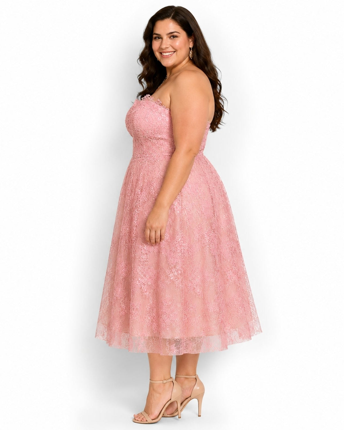 A woman modeling a strapless pink lace midi dress with a flared skirt, paired with nude high-heeled sandals, against a plain white studio background.