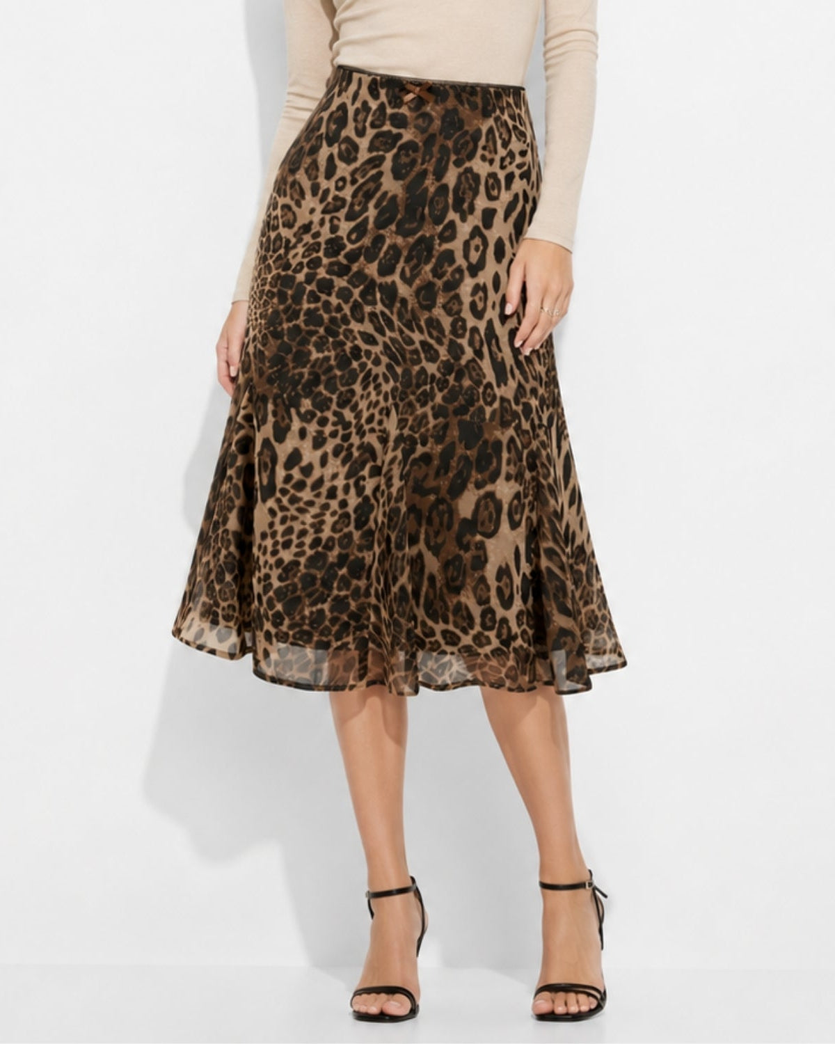 A woman models a leopard-print midi skirt with a flared silhouette, paired with a beige long-sleeve top and black strappy high-heeled sandals against a white studio background.