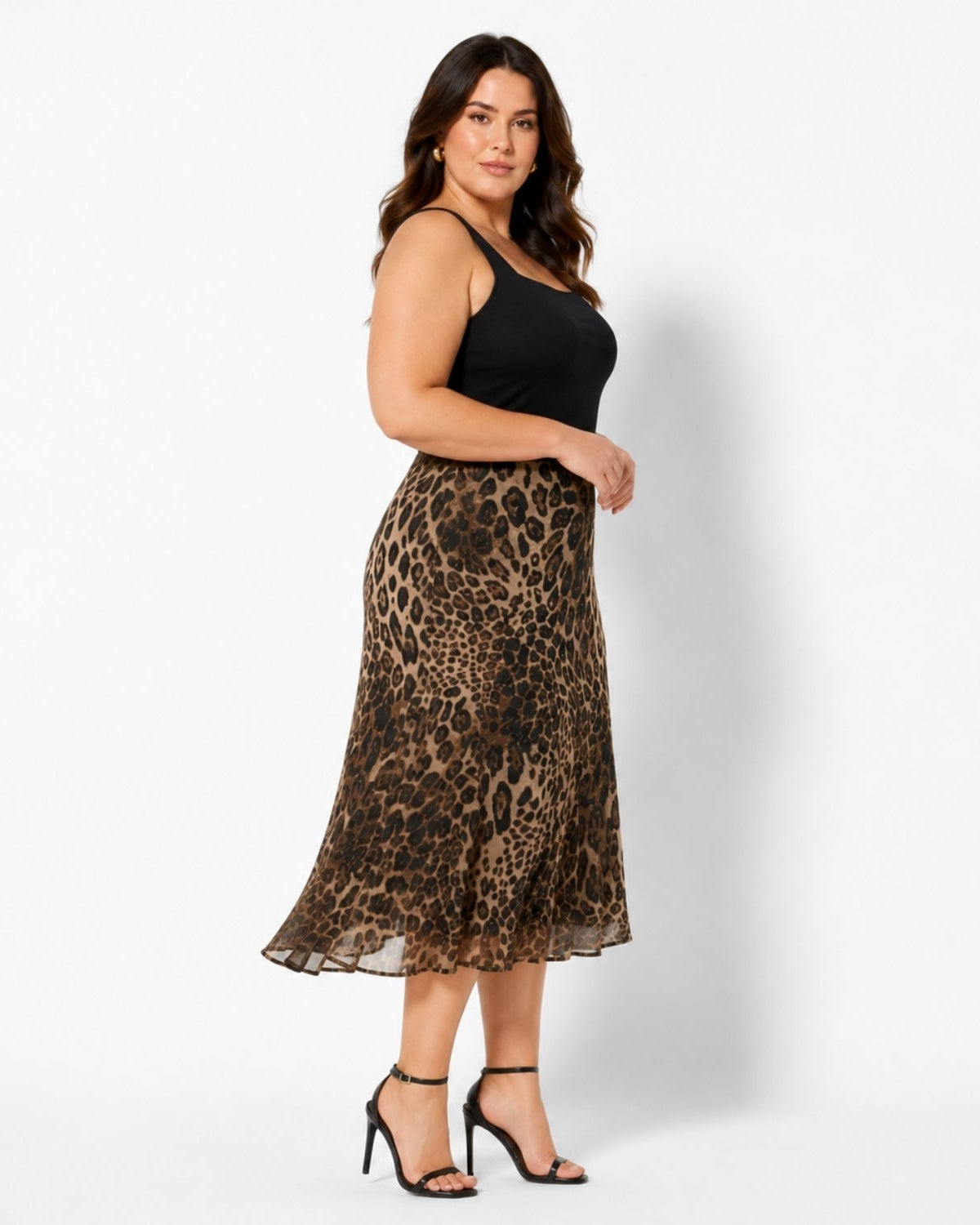 A woman modeling a black sleeveless top and a brown leopard-print midi skirt, paired with black high-heeled sandals, against a plain white studio background.