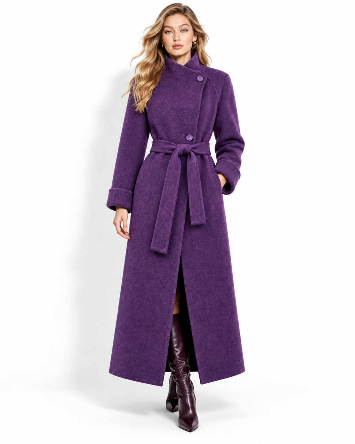 A woman modeling a long, deep purple wool coat with a belted waist and high collar, paired with dark brown leather boots, against a plain white studio background.