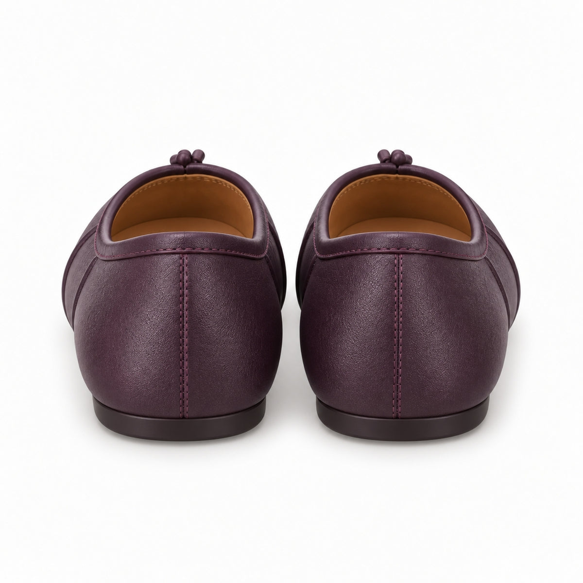 A pair of dark purple leather ballet flats shown from the back, featuring a small fabric tassel detail on the back of the shoe and a tan interior lining, set against a plain white background.