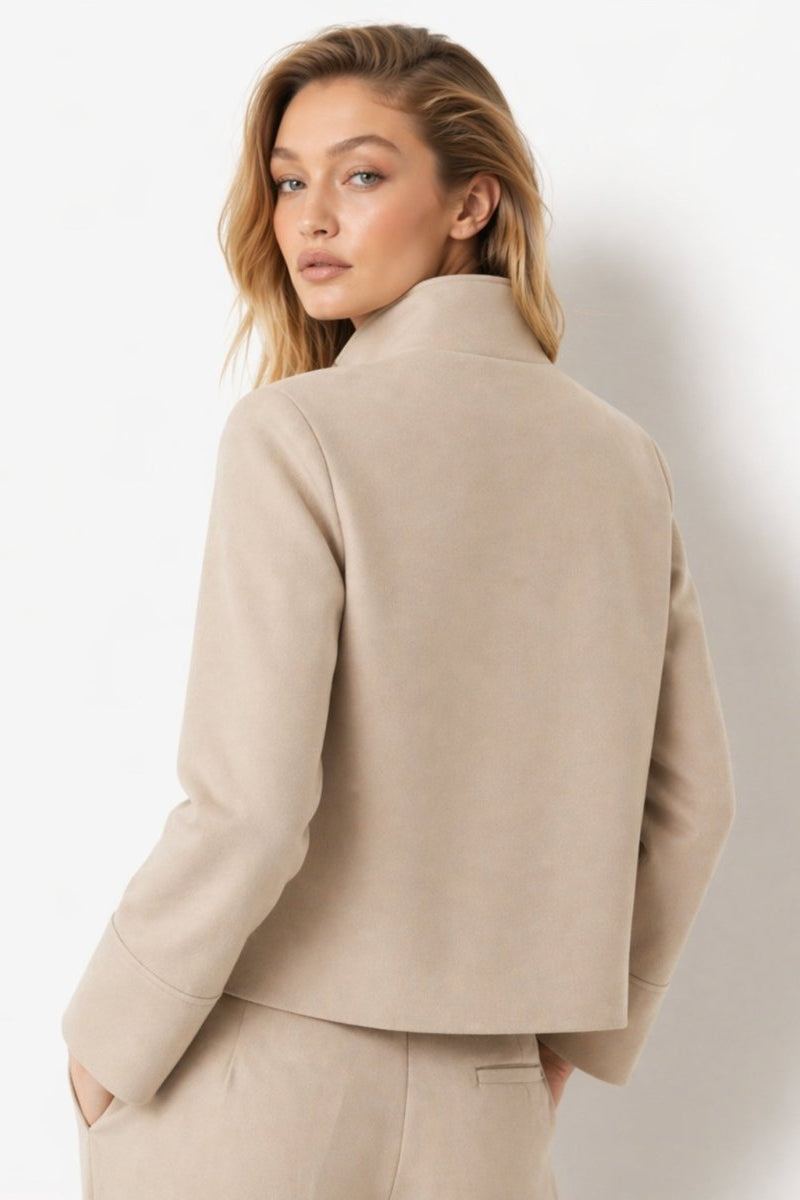 Back view of the beige funnel neck cropped outerwear jacket highlighting the clean structured tailoring.