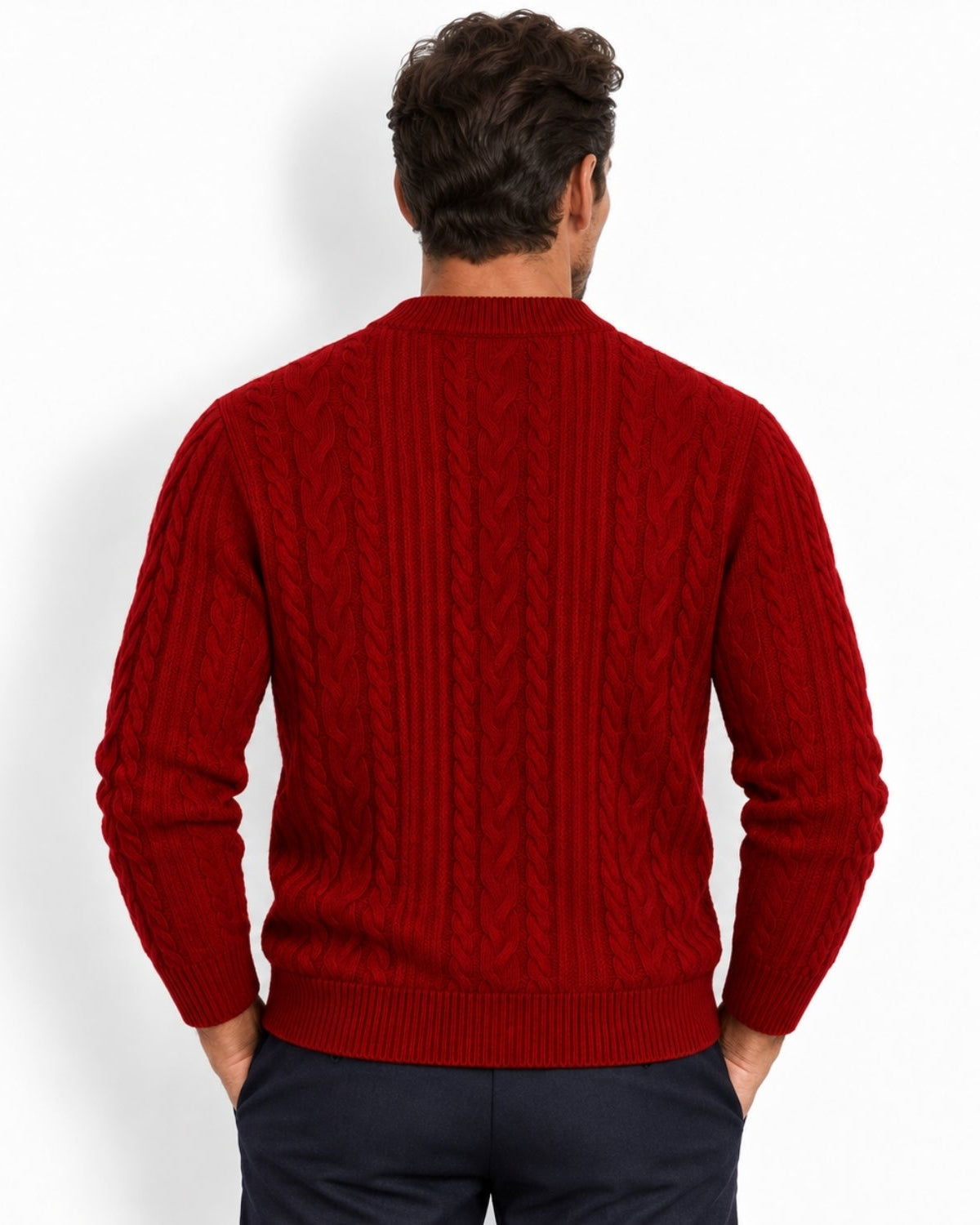A man viewed from behind wearing a red cable-knit sweater and dark navy trousers, standing against a plain white studio background.