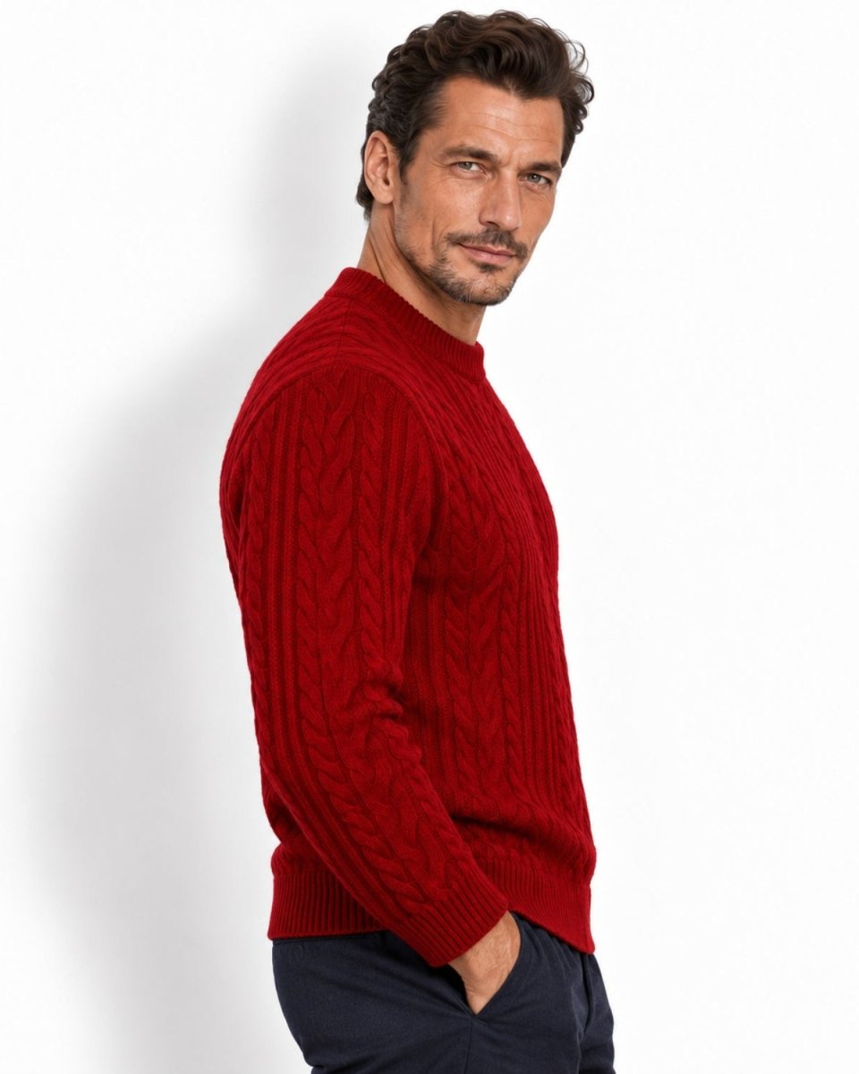A man wearing a red cable-knit sweater and dark trousers, shown in profile against a plain white studio background.