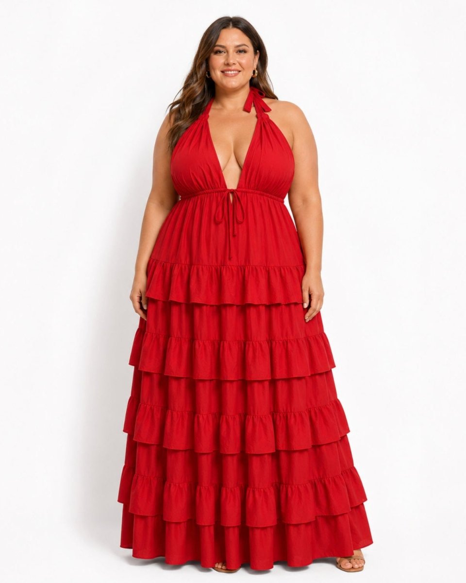 A woman modeling a bright red halter-neck maxi dress with a deep V-neckline, tie waist, and a tiered ruffled skirt, photographed against a plain white studio background.