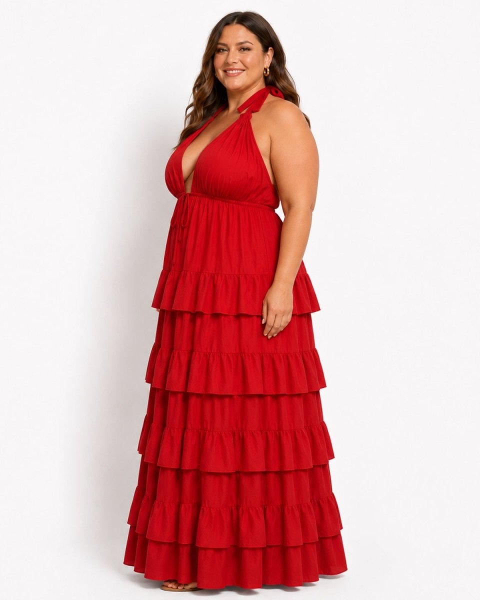 A woman modeling a red halter-neck maxi dress with a deep plunging neckline and a tiered ruffle skirt, photographed against a plain white studio background.