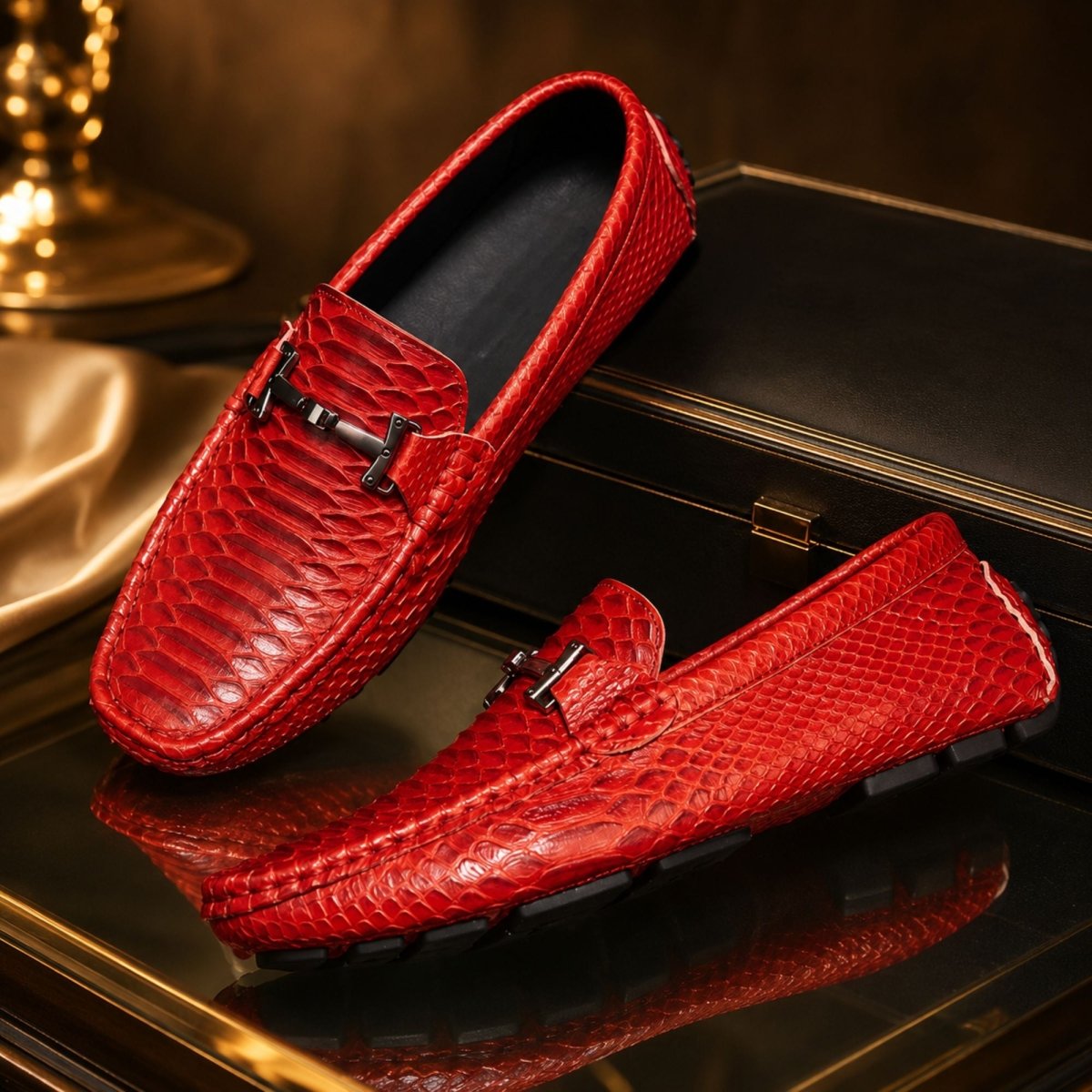 A pair of red crocodile-embossed loafers with silver-tone horsebit details, displayed on a reflective black surface with a dark leather case in the background.