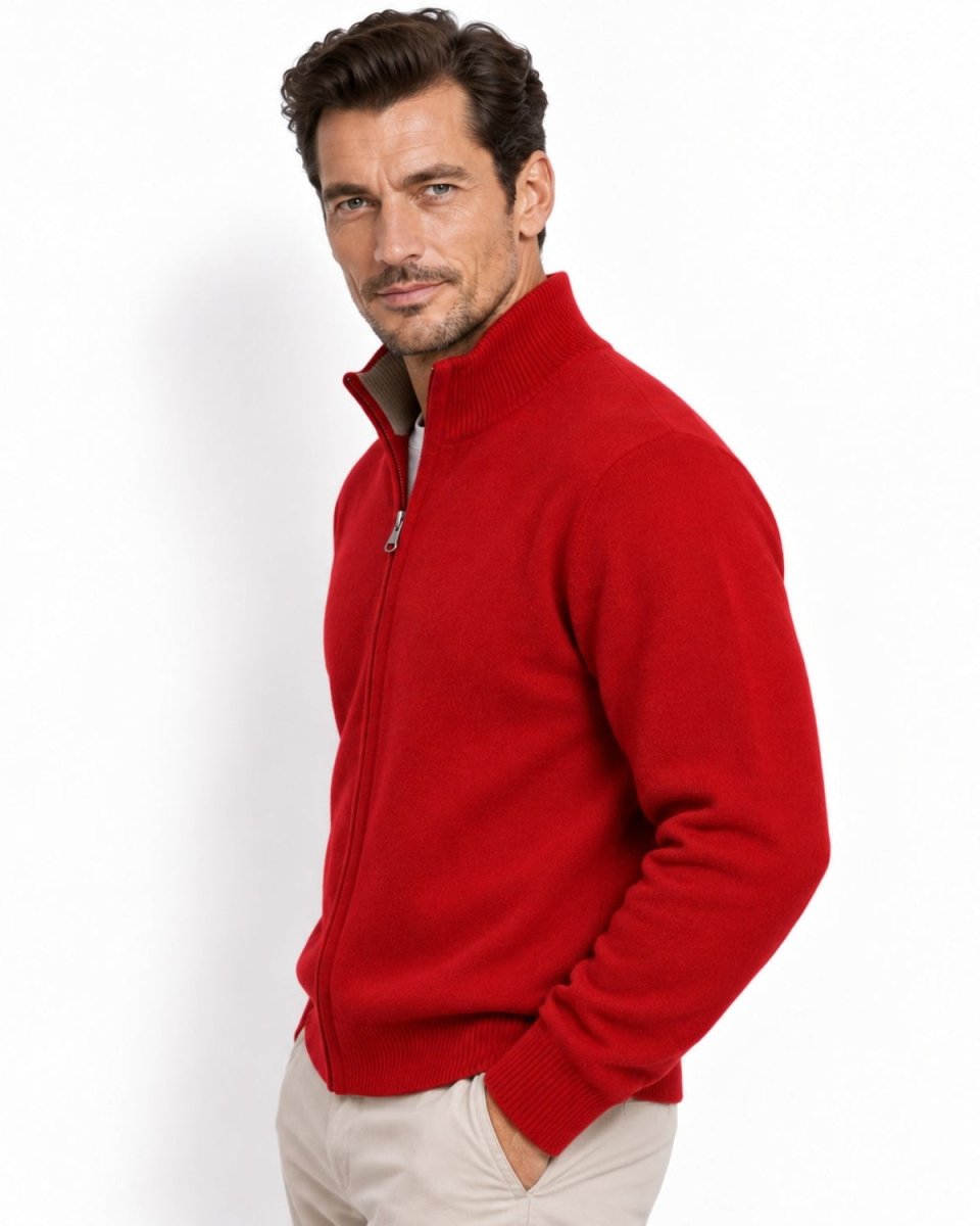 A man wearing a bright red zip-up knit sweater and light beige trousers, photographed against a clean white studio background.