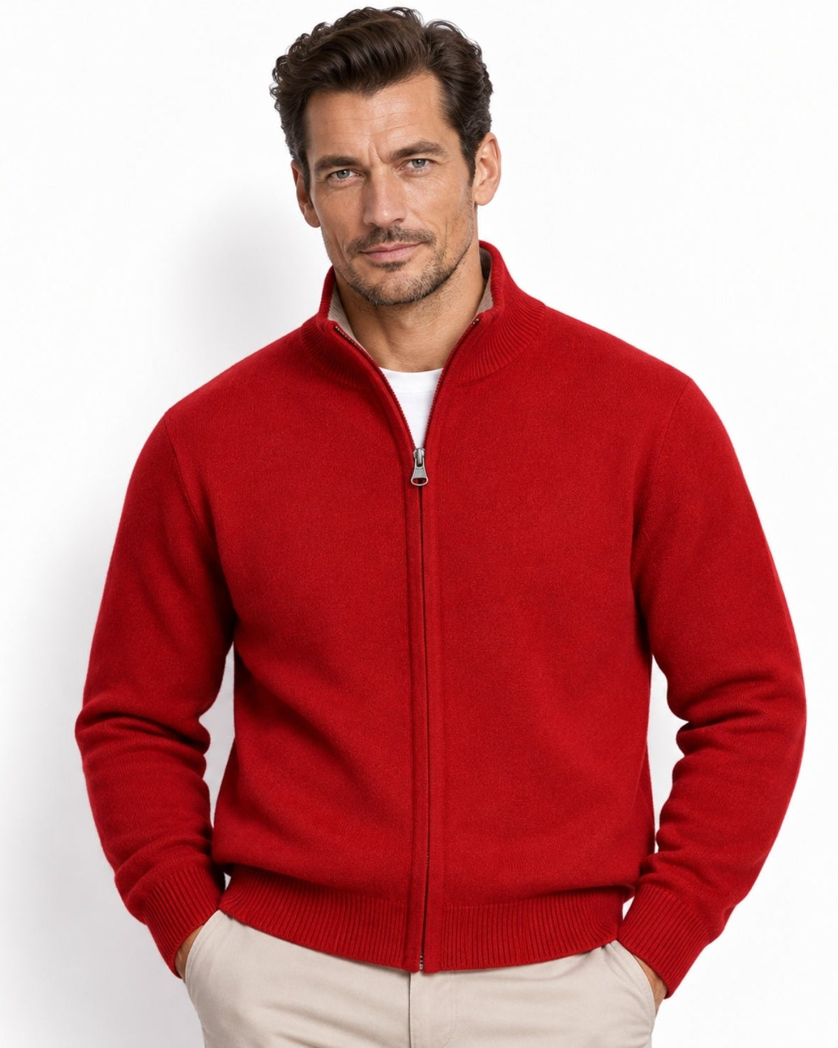 A man wearing a vibrant red knit zip-up sweater with a stand-up collar, paired with light beige trousers, photographed against a clean white studio background.