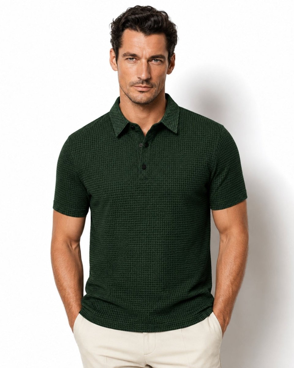 A man wearing a dark green short-sleeve polo shirt with a subtle textured pattern, paired with light beige pants, standing against a plain white studio background.