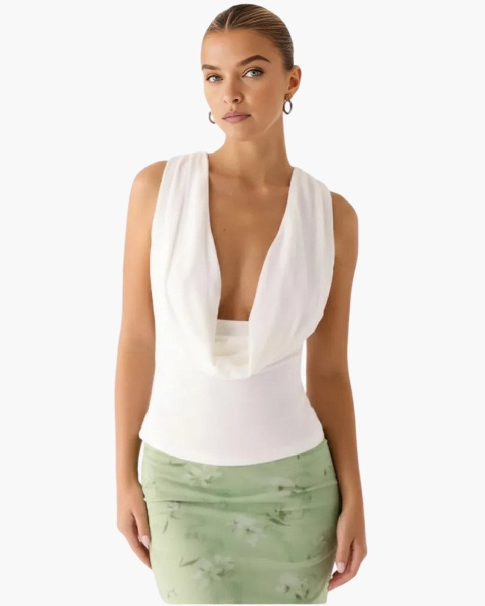 Model wearing the Rhea white sleeveless cowl neck top paired with a light green floral skirt, showing the plunging draped neckline.