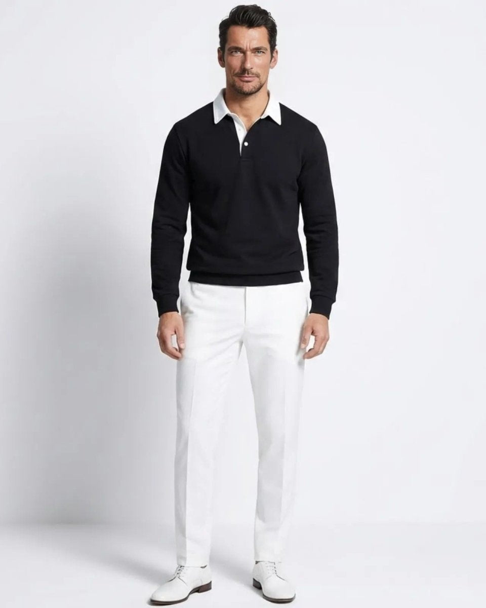 Male model wearing the Rhodes black long sleeve knit polo sweater with a white contrast collar, paired with white trousers.
