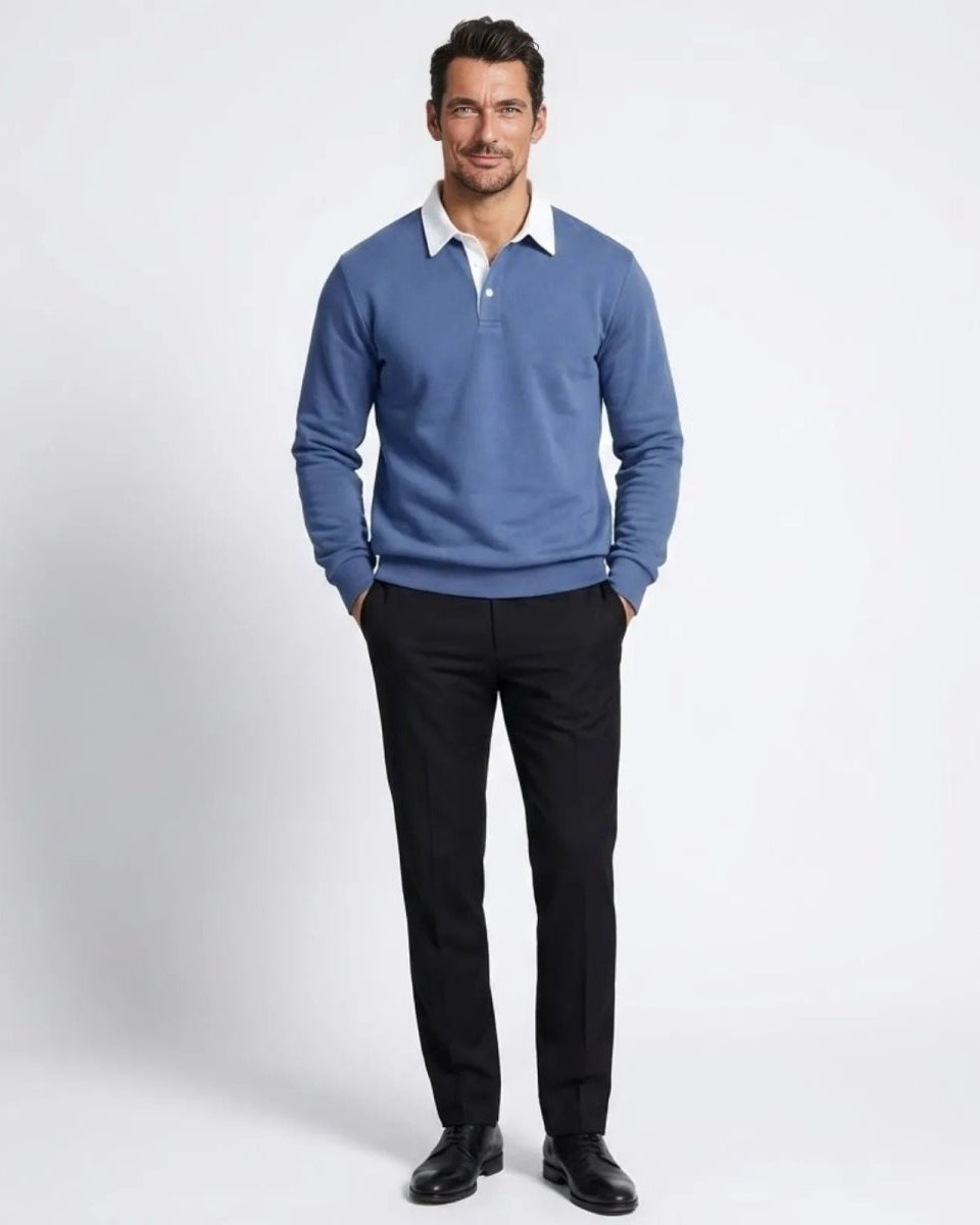 Man wearing the Rhodes long sleeve polo sweater in steel blue, styled with black dress pants and black shoes, standing against a white background.