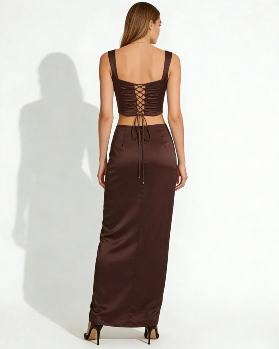 Back view of a model in the rona dark brown satin set, detailing the adjustable lace-up corset back of the top and the full length of the maxi skirt.