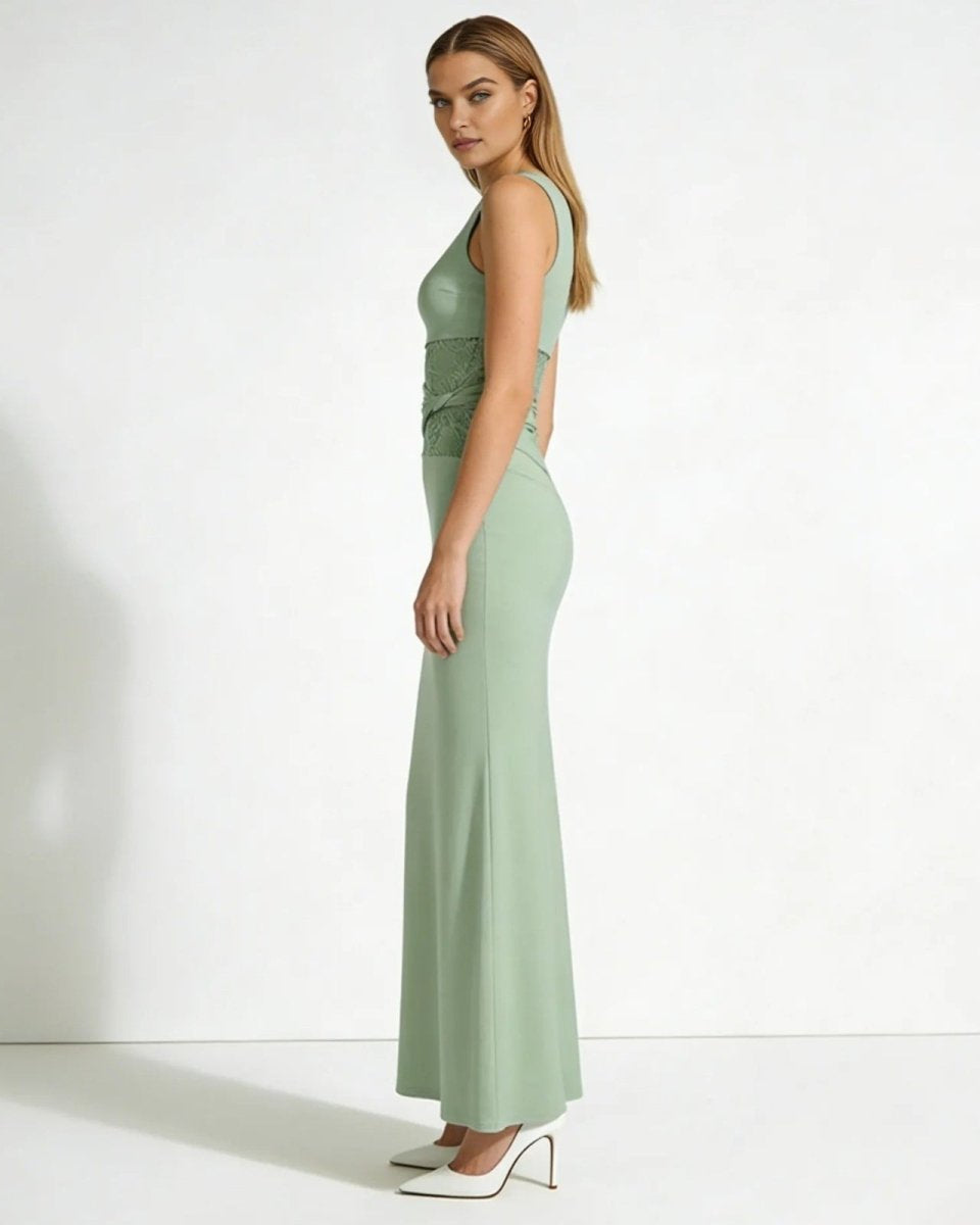 Side profile of a woman in a sage green sleeveless evening gown showing the slim column silhouette and criss-cross lace waist.
