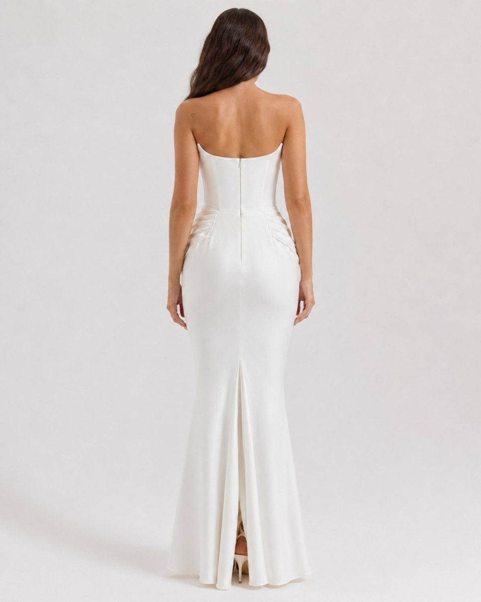 A woman viewed from the back wearing a strapless white mermaid-style gown with a fitted bodice, gathered waist, and front slit, photographed against a plain light gray studio background.