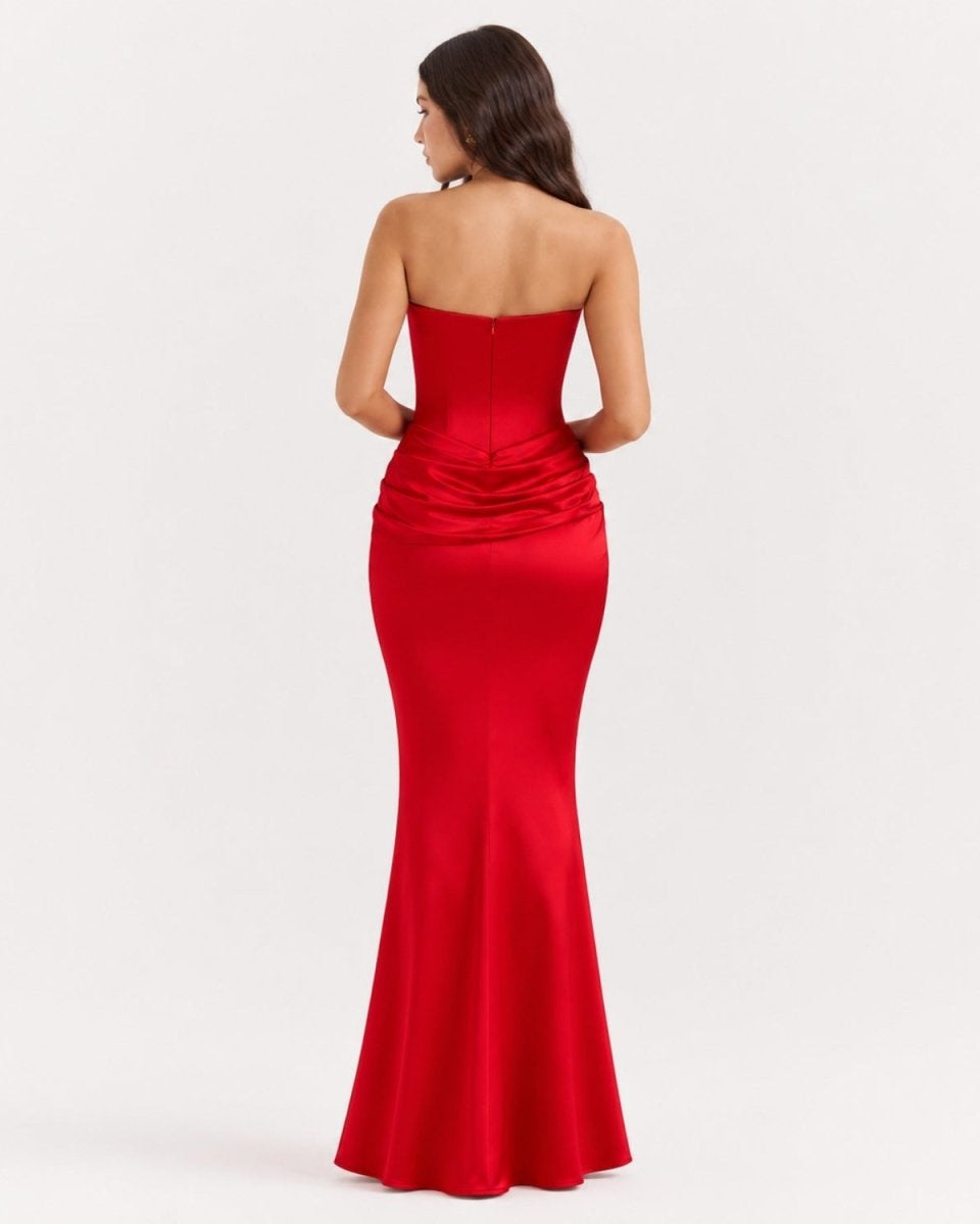 A woman viewed from the back wearing a strapless red satin mermaid gown against a plain light gray studio background.