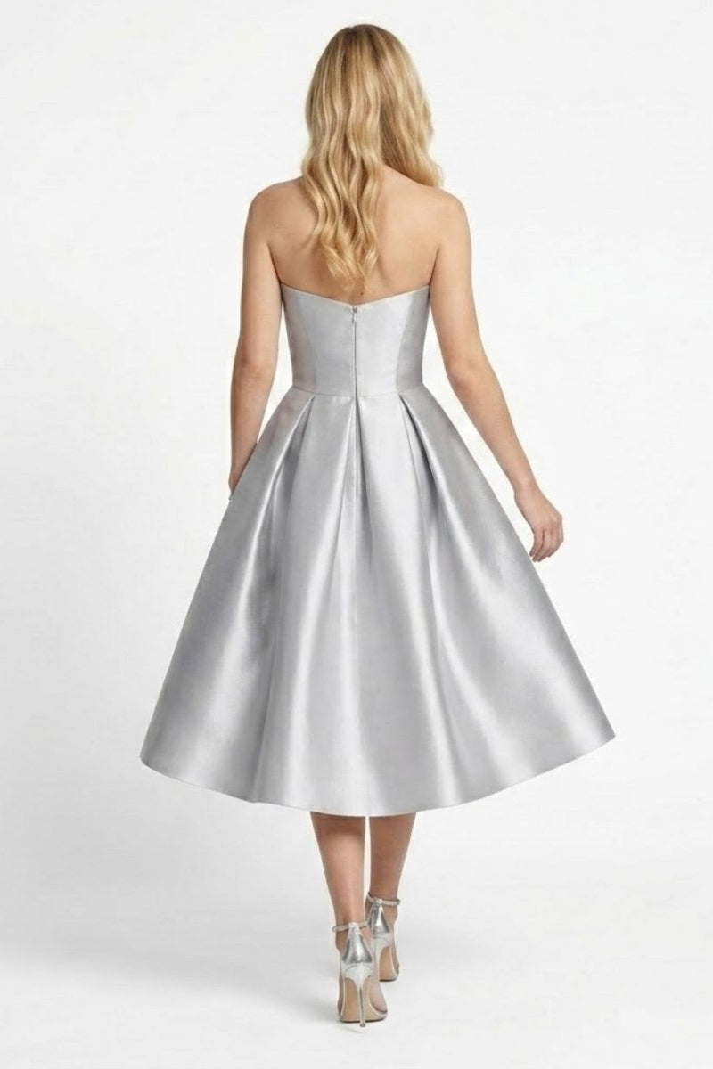 Back view of a silver strapless midi dress showing invisible back zipper and deep pleat details on the model.